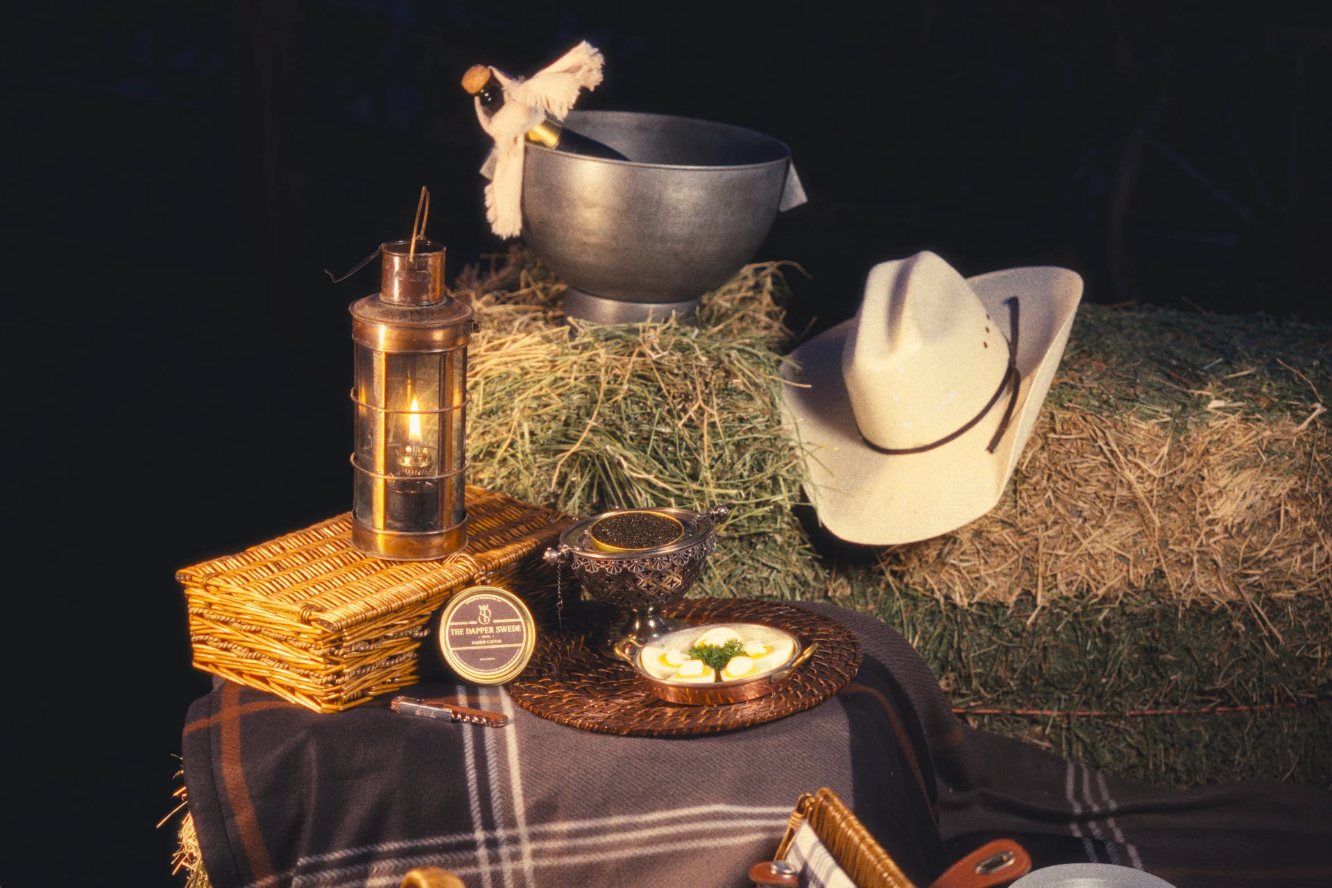 Baerii caviar with a wicker picnic basket, lantern and white cowboy hat beside hay bales