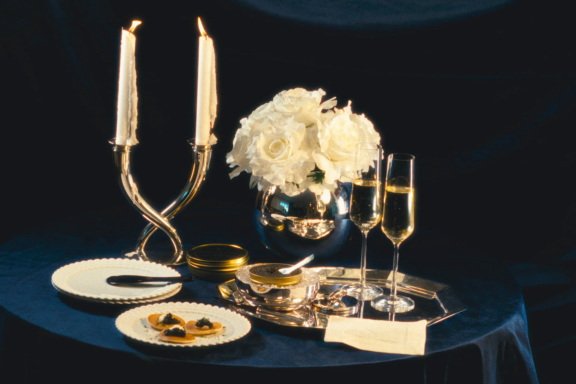 Beluga caviar on a blue table with candles, white roses and champagne