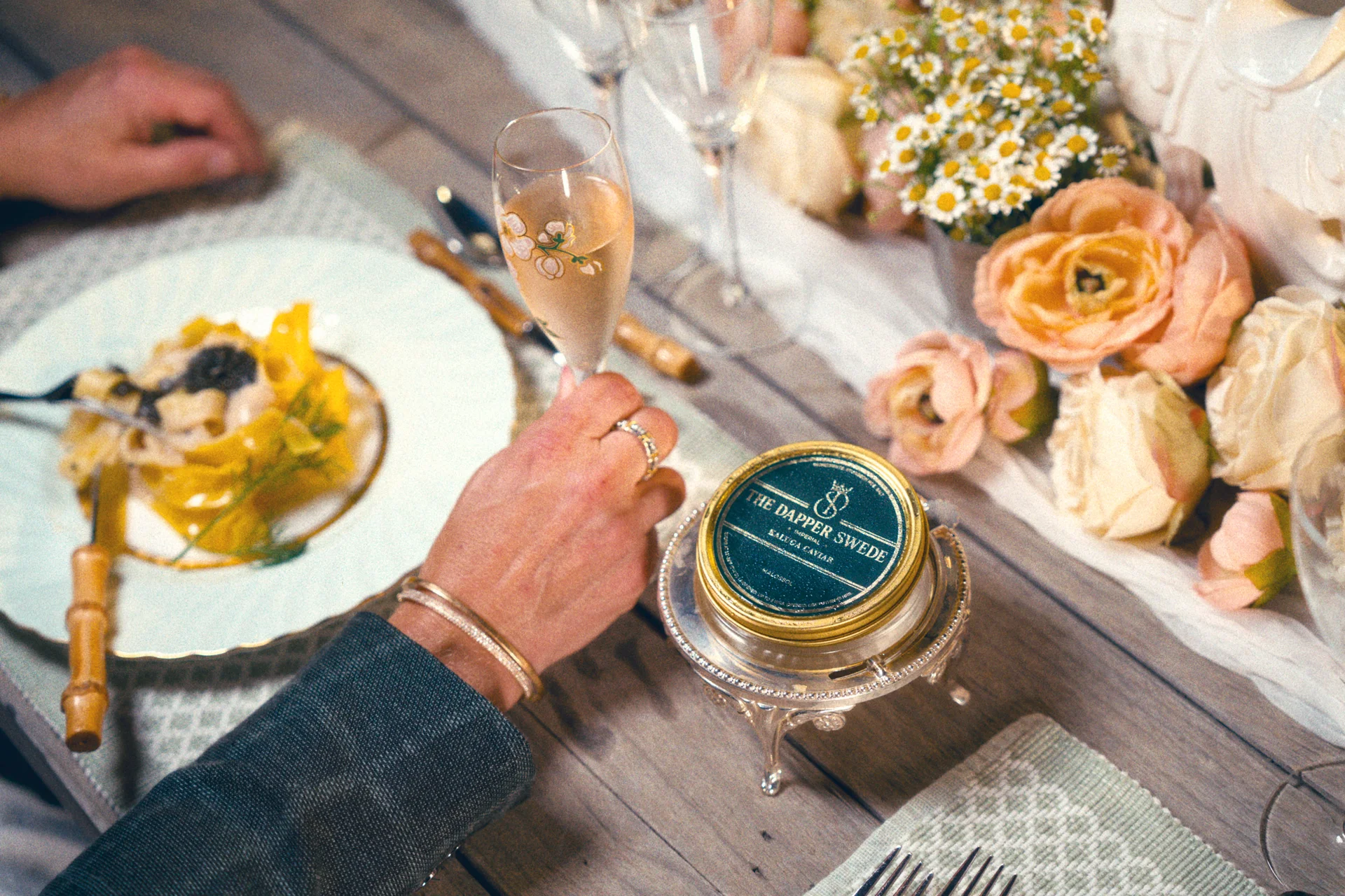 Kaluga caviar beside champagne, pasta and flowers at a garden table