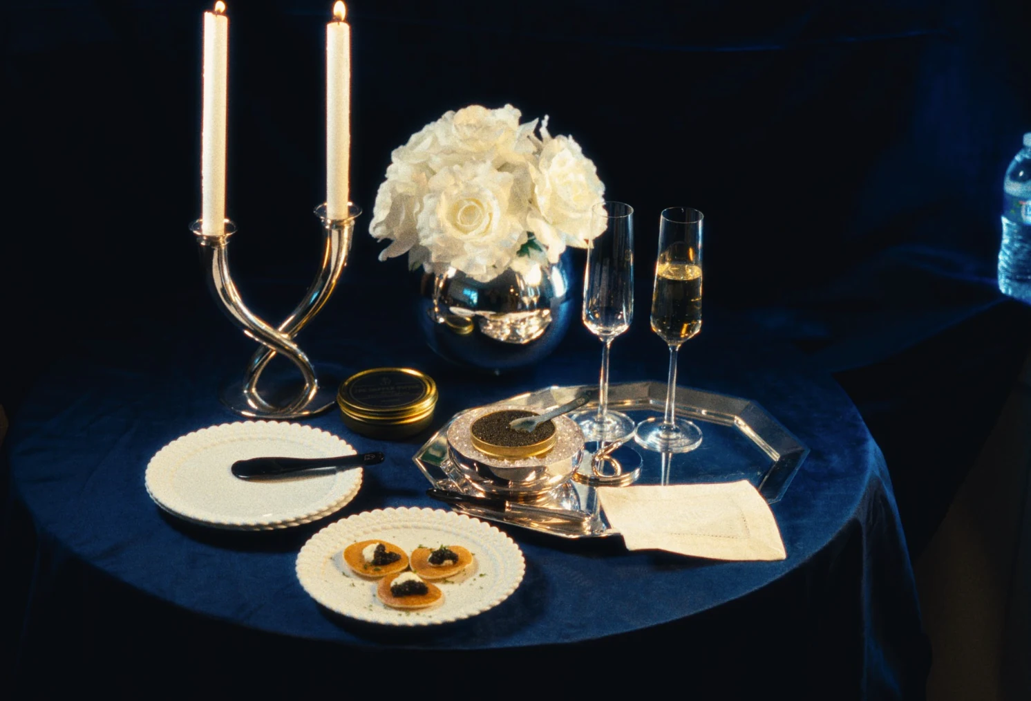 A candlelit table set with caviar, champagne and white roses